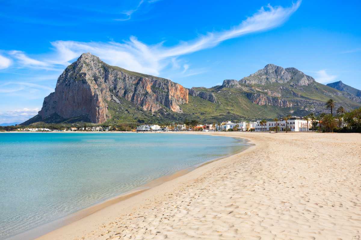 Tramonto sulla spiaggia di Macari, colori caldi, pochi bagnanti, rocce e sabbia, mare calmo, atmosfera tranquilla a San Vito Lo Capo